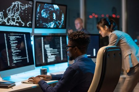 Young it-engineer decoding data while sitting in front of computer monitors and looking at screen of one of them